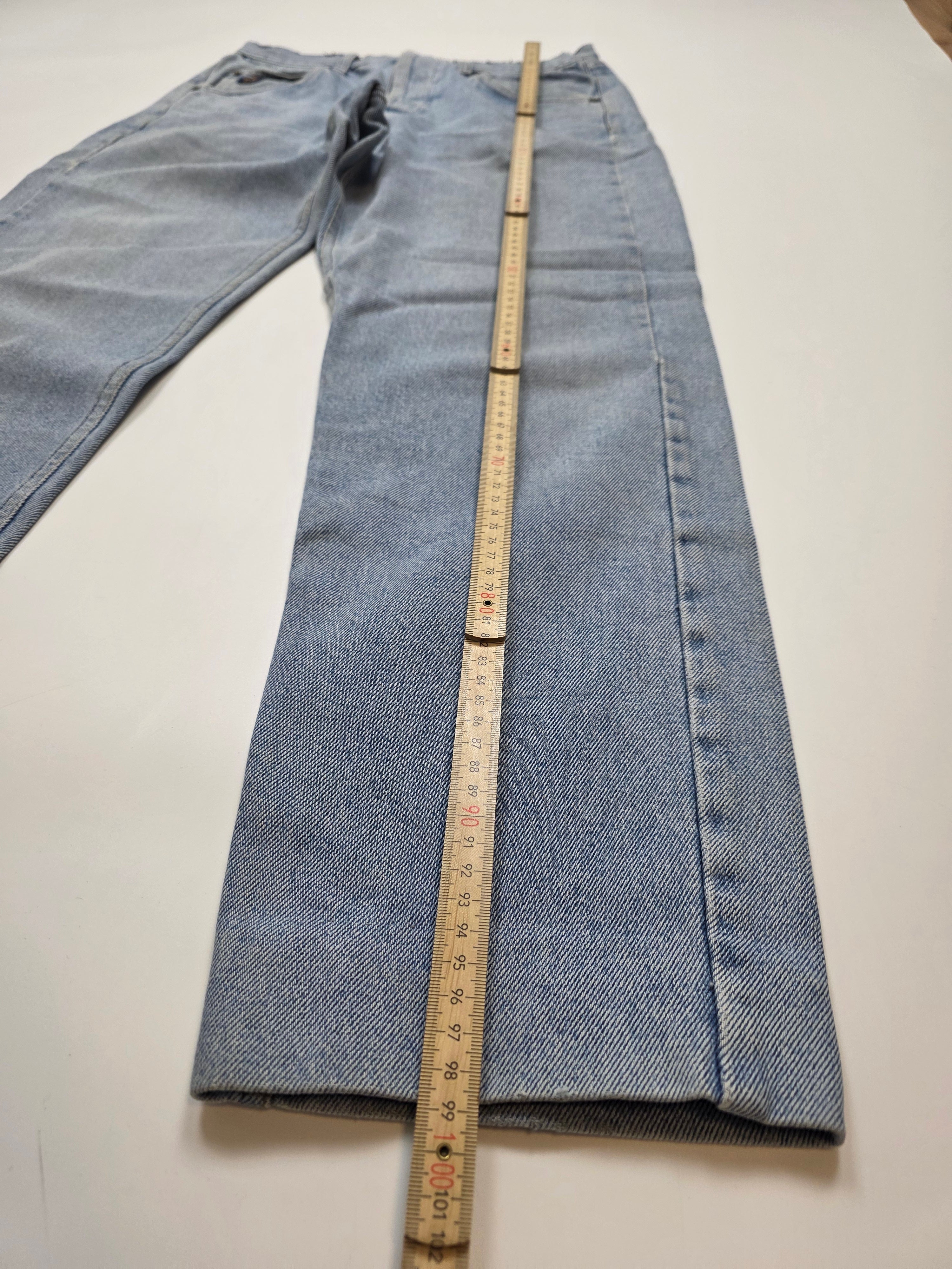 Vintage Jeans in Hellblau mit Maßband zur Längenmessung, flach auf weißem Hintergrund