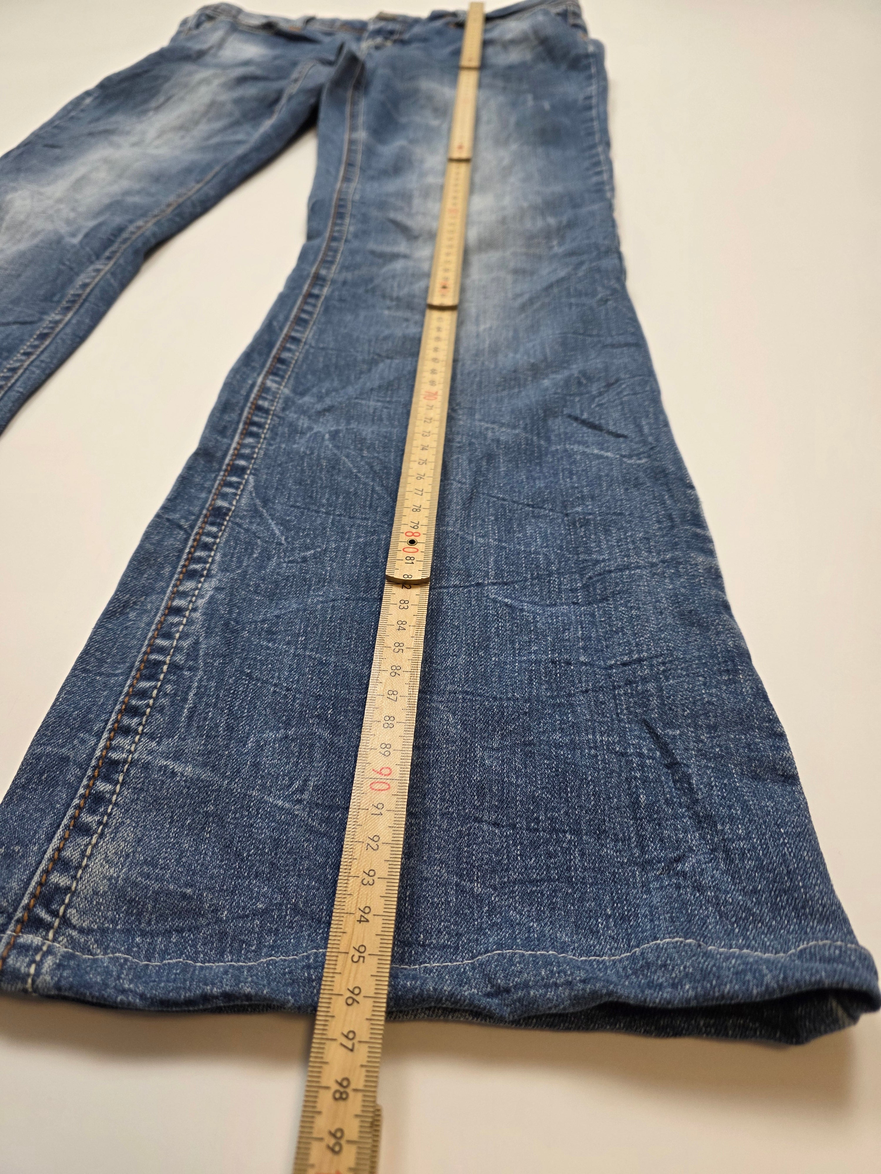Vintage Jeanshose mit Lineal zur Längenmessung auf weißem Hintergrund, Used-Look, Y2K-Style