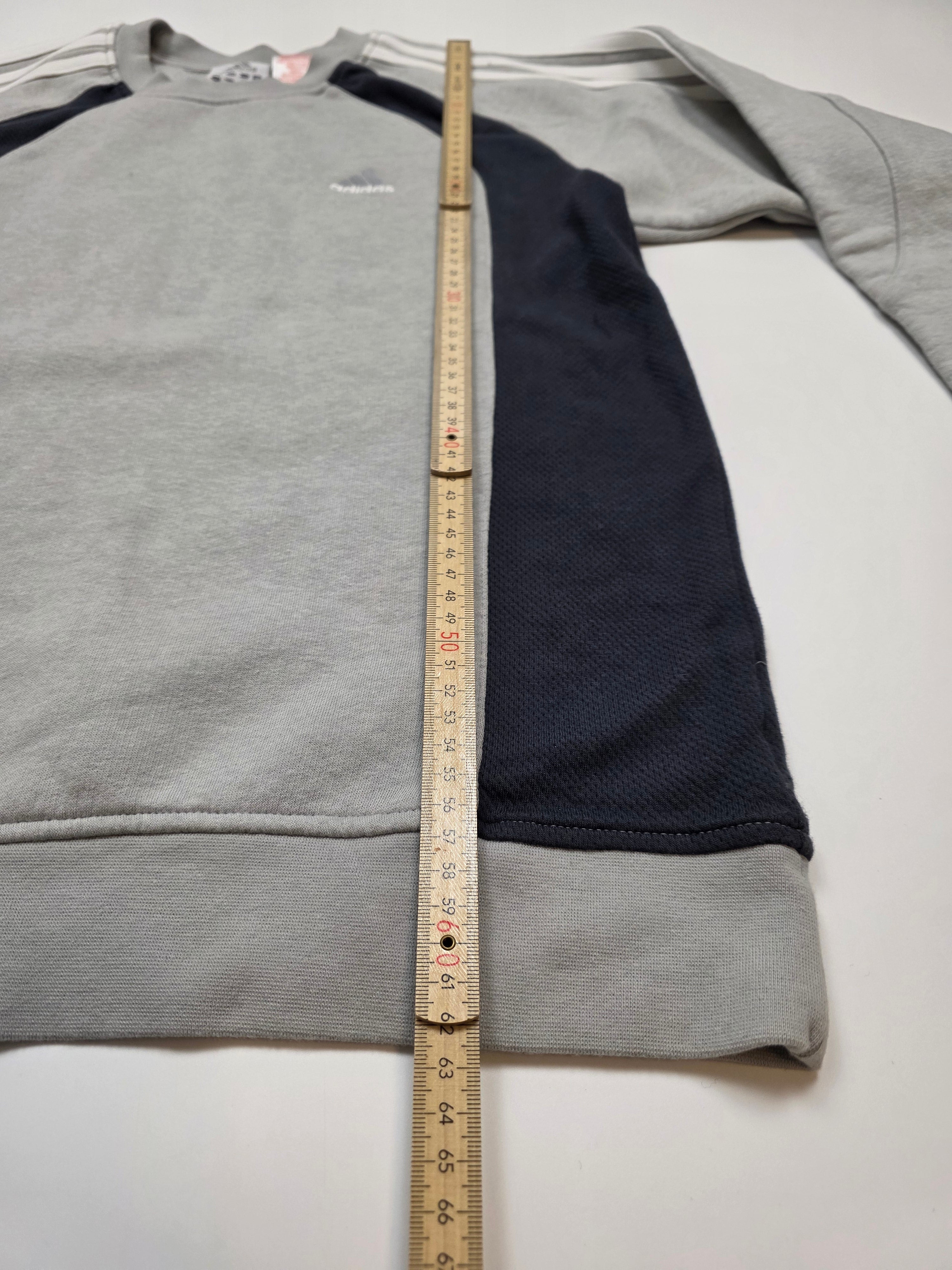 Grauer Vintage-Sweater mit dunklen Ärmeln, Maßband zur Längenmessung auf weißem Hintergrund