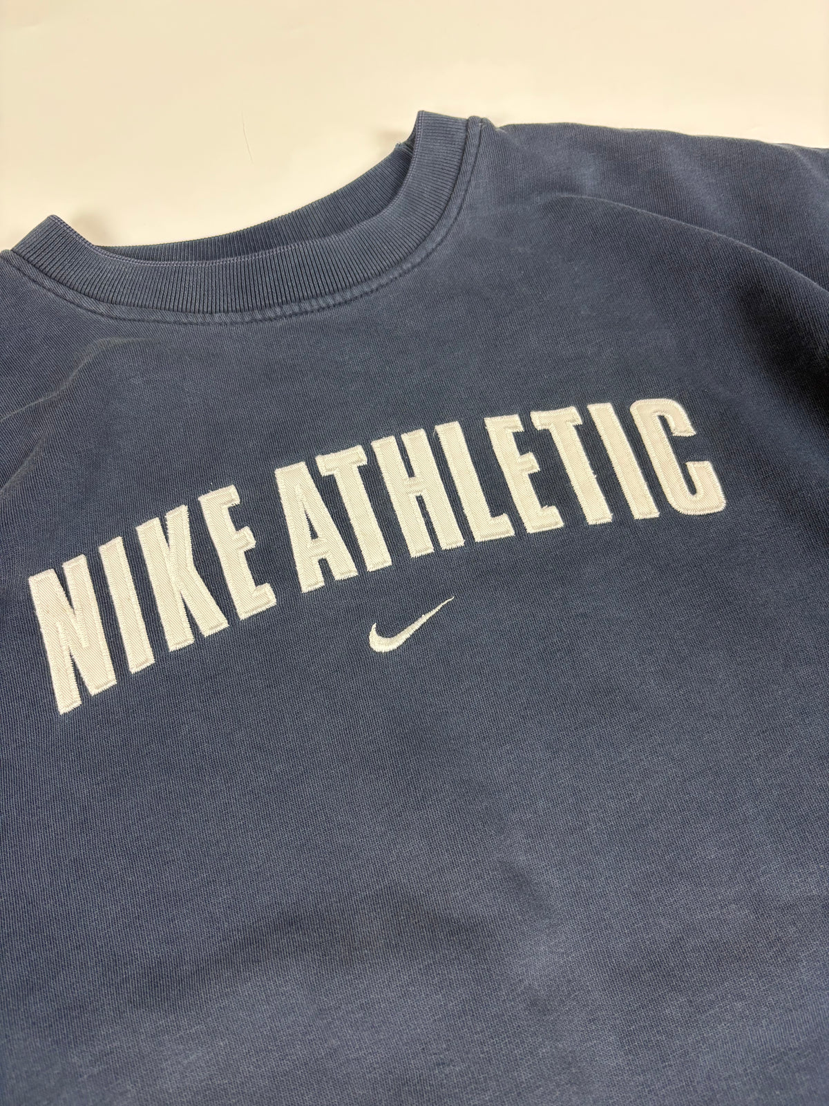 Nahaufnahme des gestickten NIKE-ATHLETIC-Schriftzugs in Creme mit kleinem Swoosh am Rippkragen