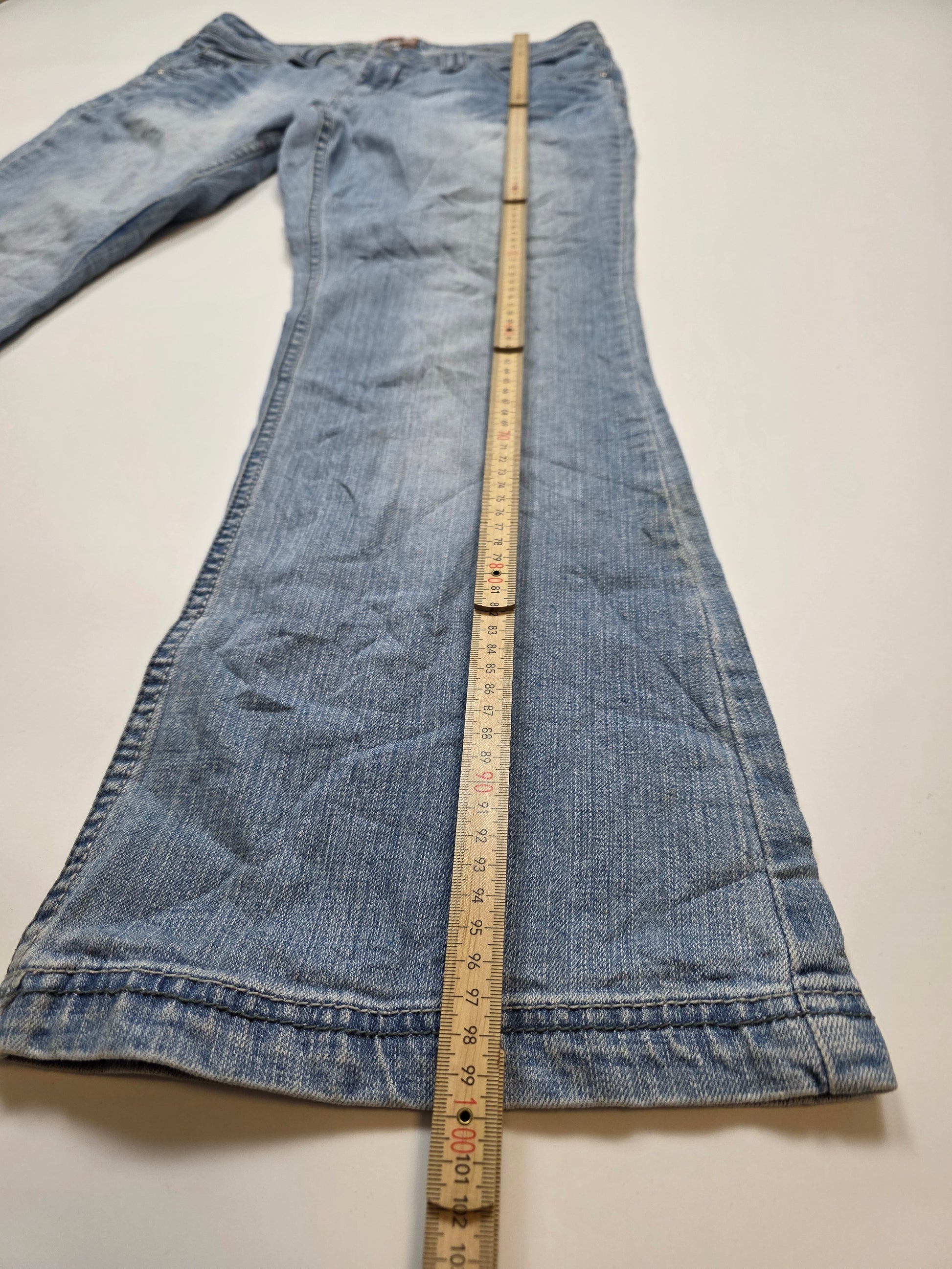 Vintage Jeanshose in Hellblau mit Maßband auf weißem Hintergrund, Beinlänge wird gemessen