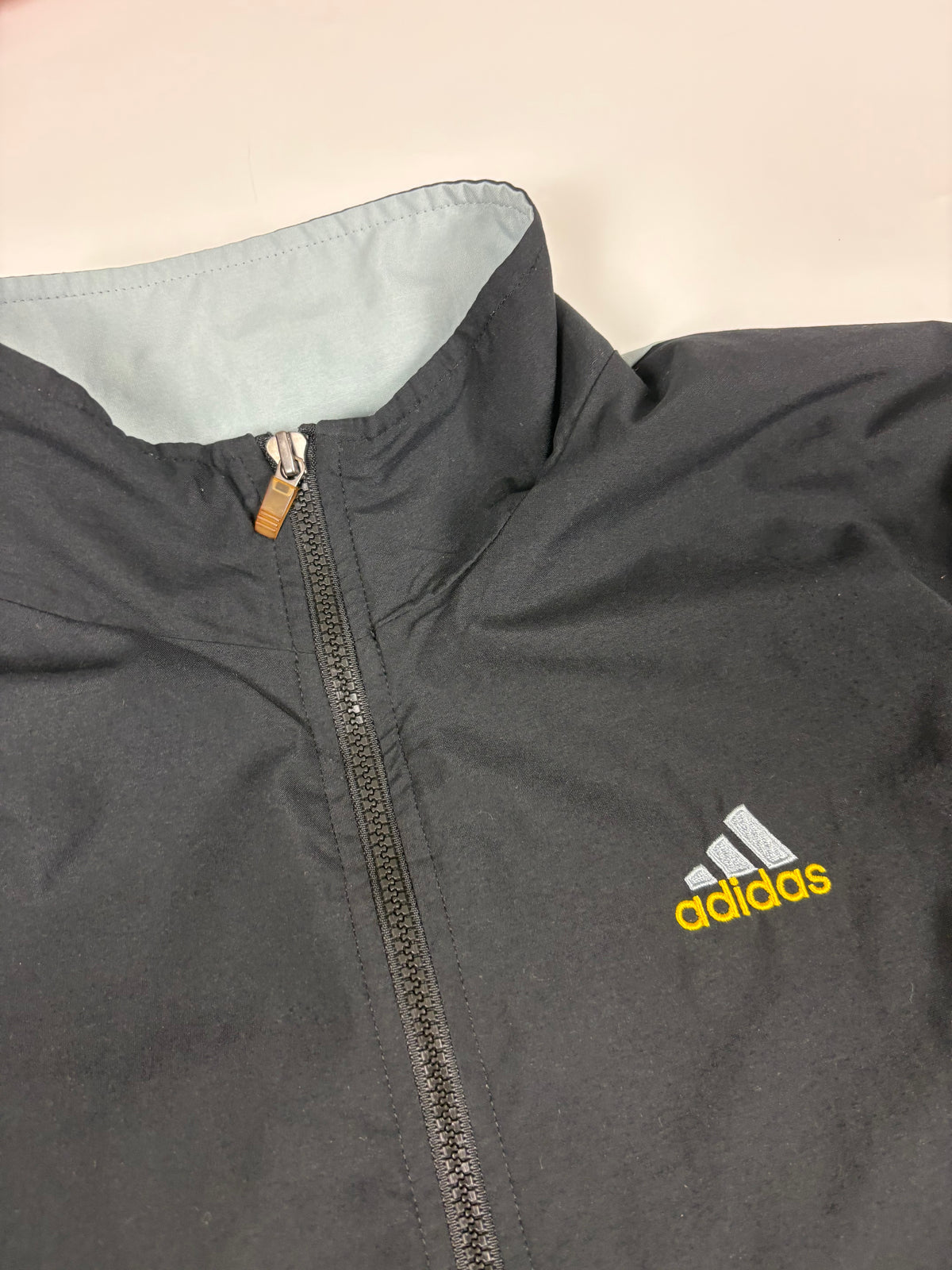 Stehkragen mit hellgrauem Innenkragen, braunem Reißverschluss-Zipper und gesticktem gelb-grauem Adidas-Logo