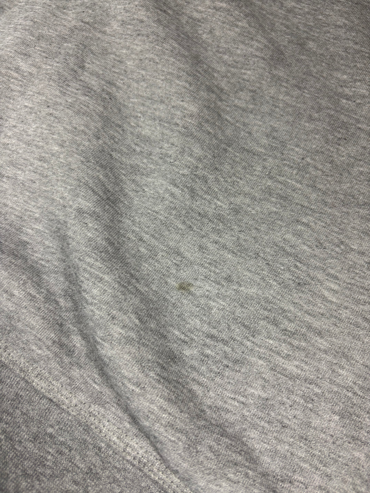 Nahaufnahme von grauem Melange-Stoff mit kleinem hellem olivfarbenem Fleck nahe dem Saum