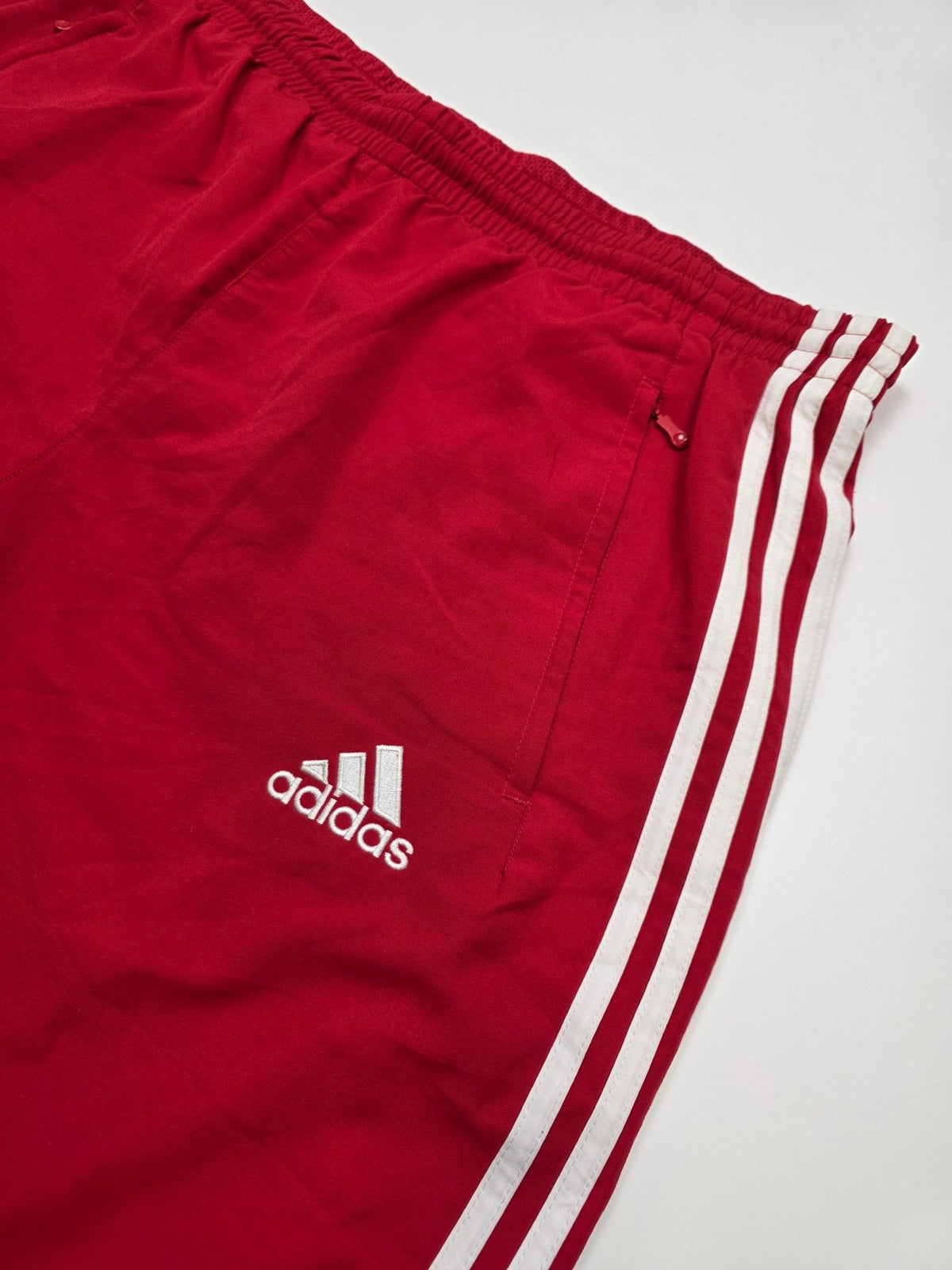 Detail des weißen Adidas Performance Logos, der Zip-Tasche und 3-Streifen an den roten Ajax Trackpants