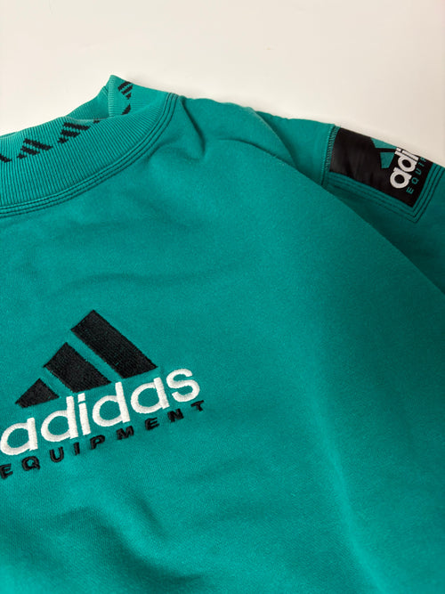Nahaufnahme von Brust-Stickerei, Schulter und Stehkragen mit Dreistreifen-Muster am grünen Adidas Equipment Sweater