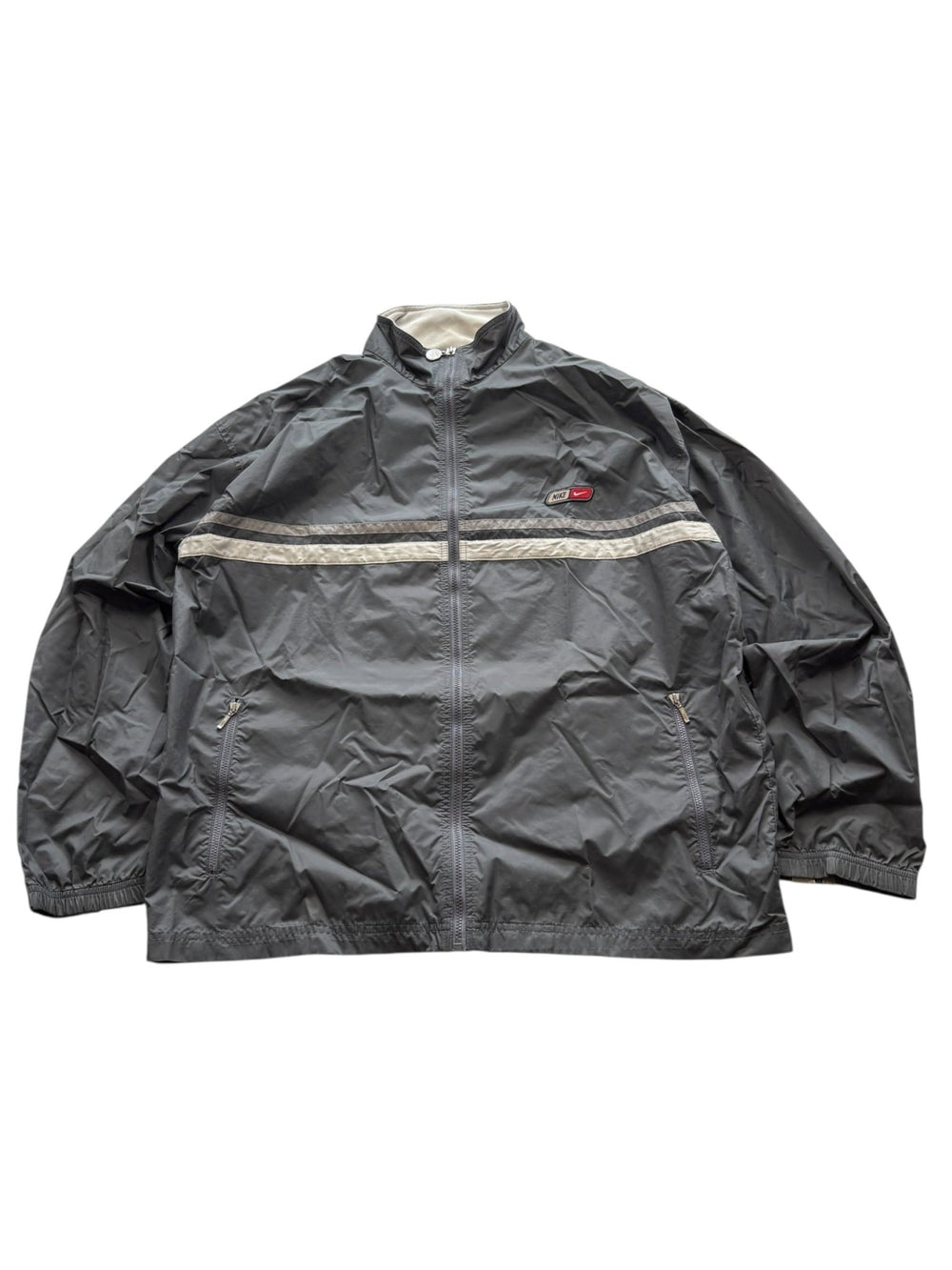 Graue Nike 00s Vintage Trackjacket mit Reflektorstreifen und kleinem Patch-Logo auf der Brust