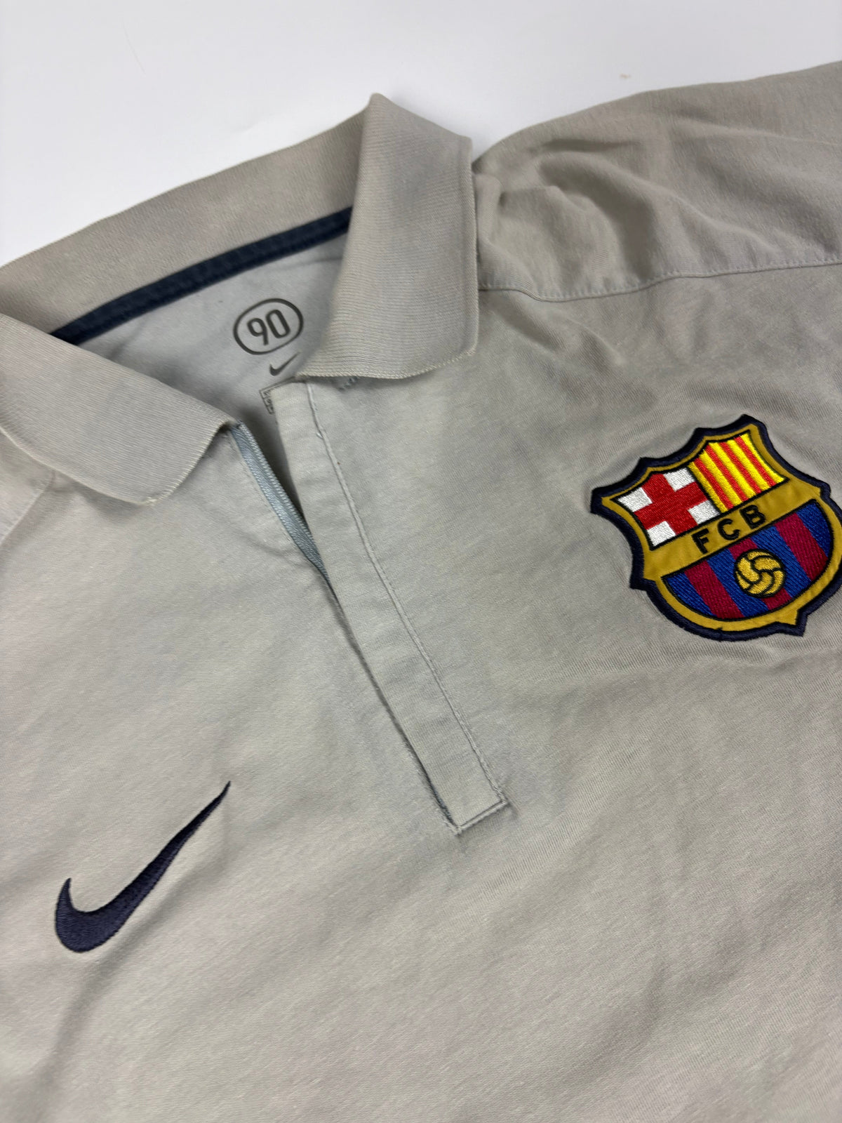 Kragen mit dunkelblauer Paspel, kurzer Reißverschlussleiste, FCB-Wappen und Nike-Swoosh am grauen Poloshirt