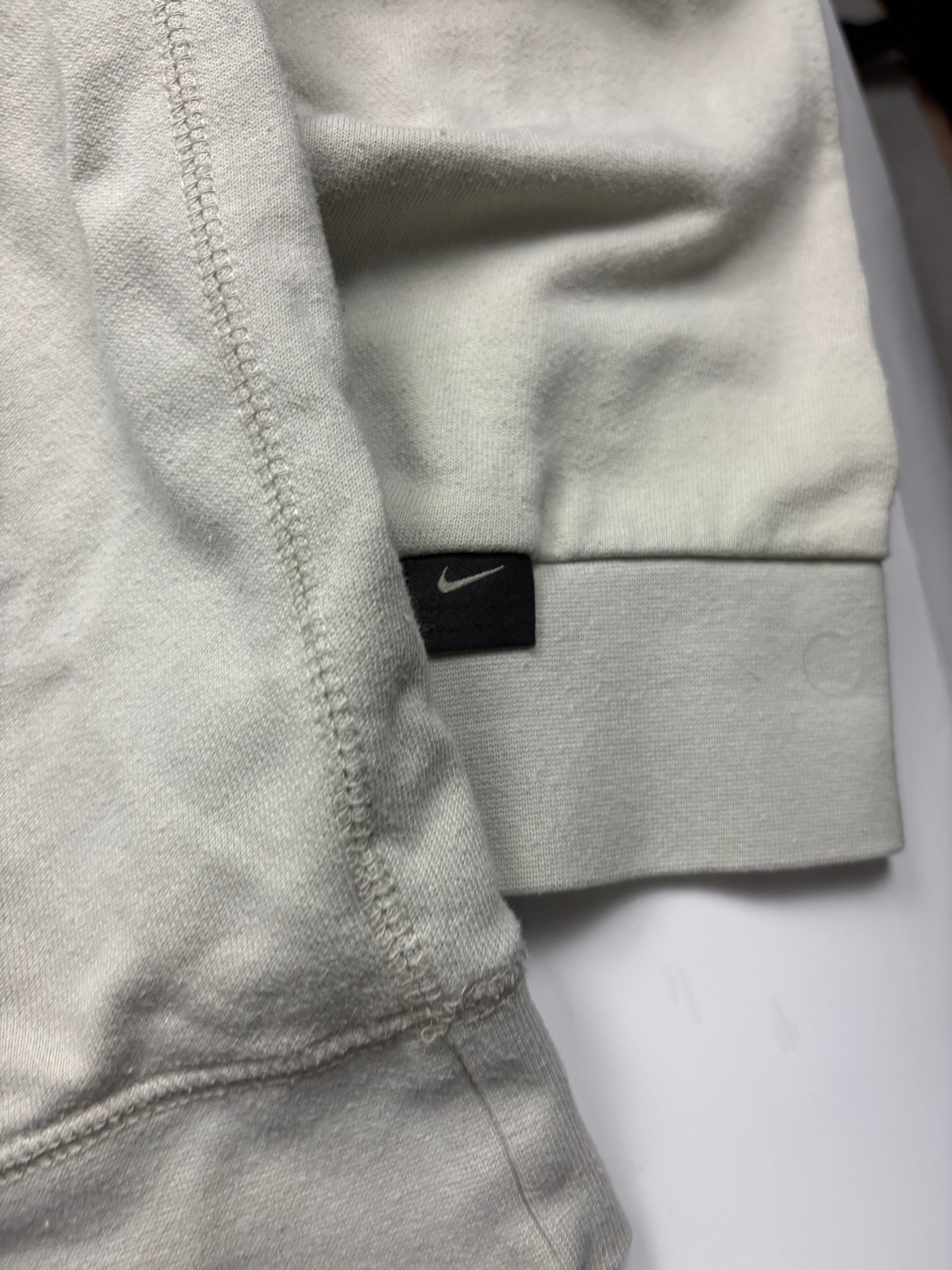 Schwarzes Nike Swoosh Label am Ärmelbündchen des hellgrauen Vintage Sweaters
