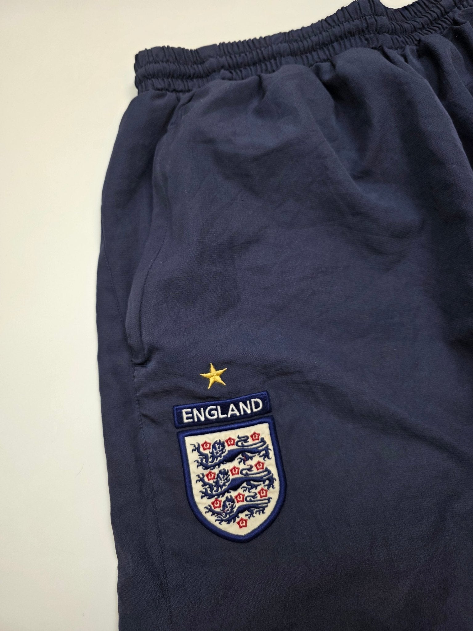 Detail des England Three Lions Wappens mit goldenem Stern an den navyfarbenen Umbro Vintage Trackpants