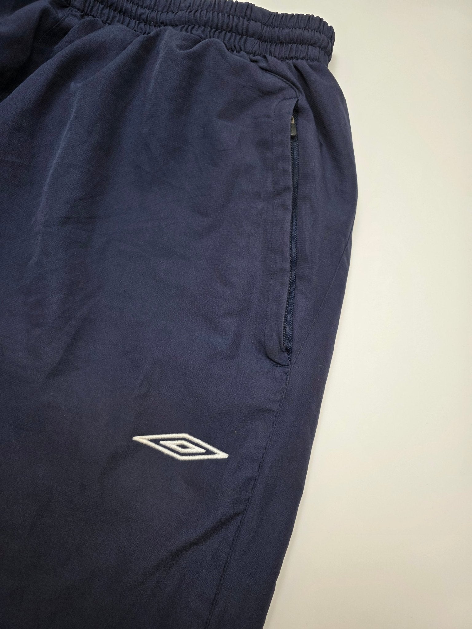 Detail des weißen Umbro Logos und der Zip-Tasche an den England Vintage Trackpants in Navy